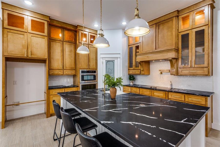 Kitchen with a kitchen bar, a kitchen island, pendant lighting, stainless steel double oven, and dark stone counters