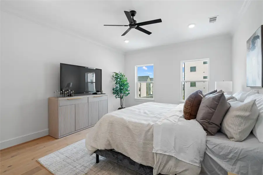 This generous third-floor primary suite showcases a king-sized bed and a stylish media setup, offering a luxurious balance of comfort, function, and modern design.