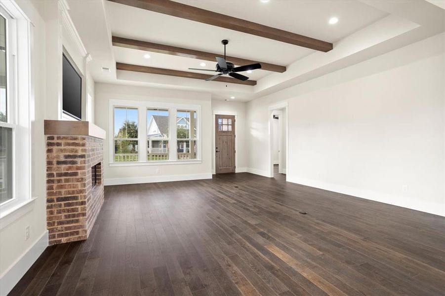 Unfurnished living room featuring dark wood-type flooring, ceiling fan, beamed ceiling, and a brick fireplace