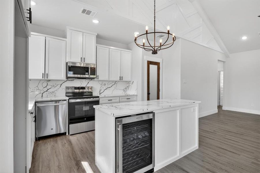 Modern kitchen featuring white cabinetry, stainless steel appliances, a center island with a built-in beverage cooler, and a vaulted ceiling with exposed beams
