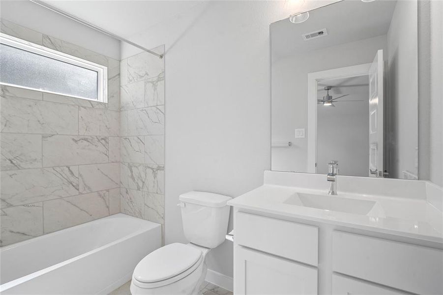 Secondary bath features tile flooring, bath/shower combo with tile surround, white stained wood cabinets, beautiful light countertops, mirror, dark, sleek fixtures and modern finishes.