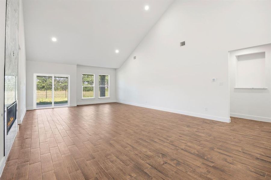 Spacious living area featuring vaulted ceilings, wood-finish flooring, an integrated fireplace with a stone-finish surround, recessed lighting, and a sliding glass door leading to the exterior Spacious living area featuring vaulted ceilings, wood-finish flooring, an integrated fireplace with a stone-finish surround, recessed lighting, and a sliding glass door leading to the exterior