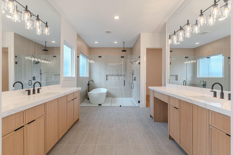 This modern bathroom features a spacious layout with dual vanities, sleek black fixtures, and ample lighting. It includes a freestanding tub and a large glass-enclosed shower, offering a luxurious, spa-like atmosphere.