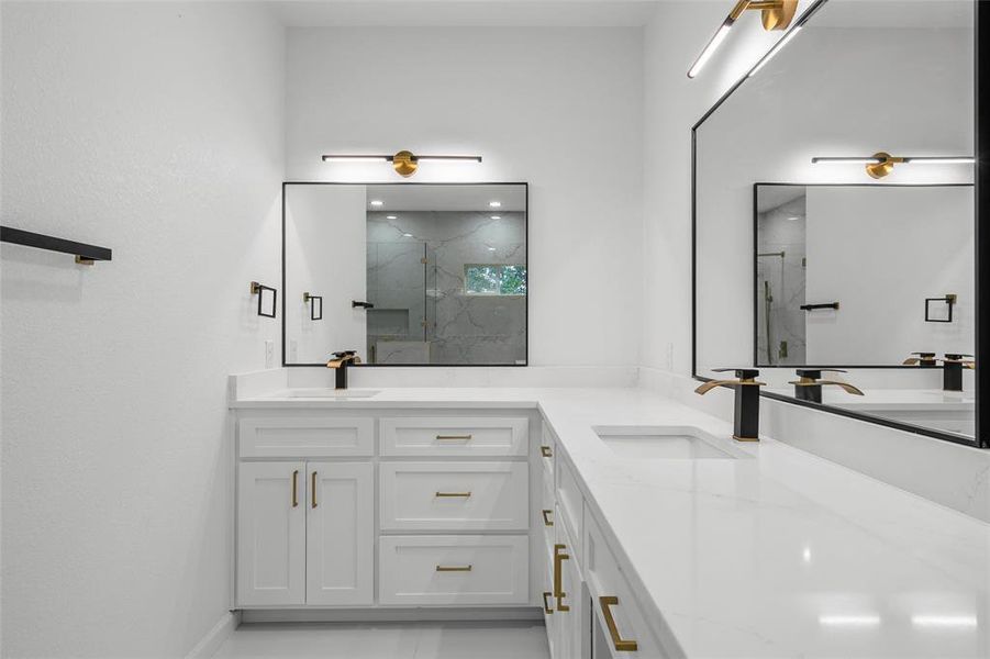 Double vanity featuring white cabinetry, integrated sinks, white countertops, black and gold fixtures, and rectangular mirrors with black frames Double vanity featuring white cabinetry, integrated sinks, white countertops, black and gold fixtures, and rectangular mirrors with black frames