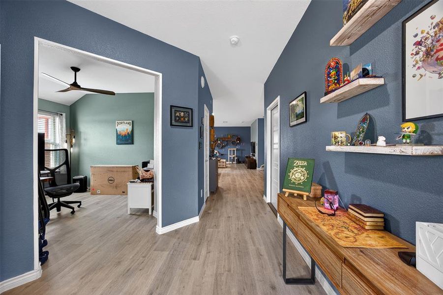 Hall featuring a desk, light wood-style floors, a textured wall, and vaulted ceiling