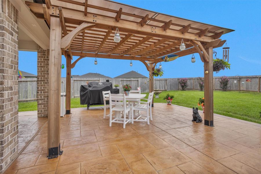 This photo shows a spacious backyard patio with a wooden pergola, and a well-maintained lawn.