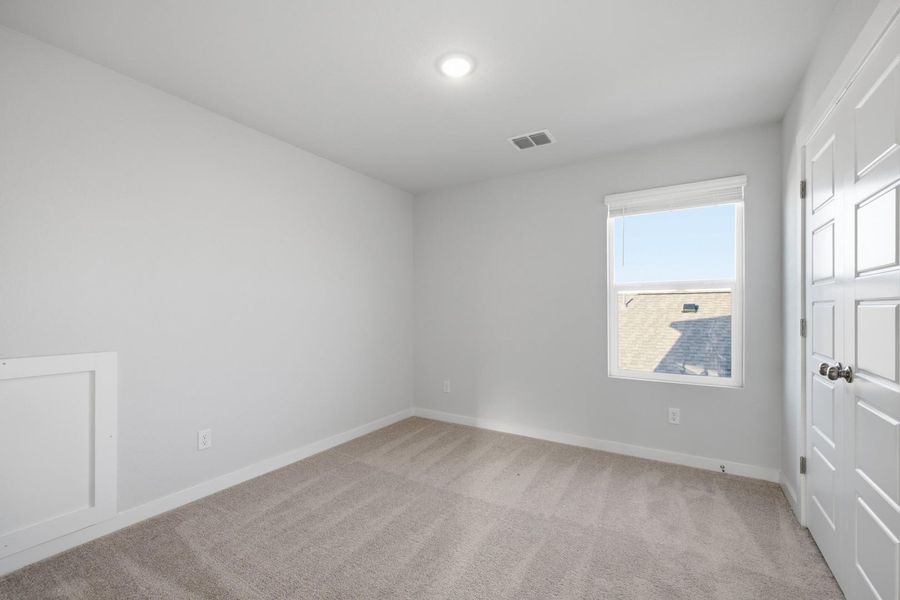A well-lit bedroom features plush carpeting and a bright window offering views of the neighborhood.