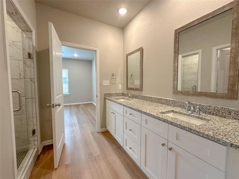 Bathroom with hardwood / wood-style flooring, double vanity, and a shower with door