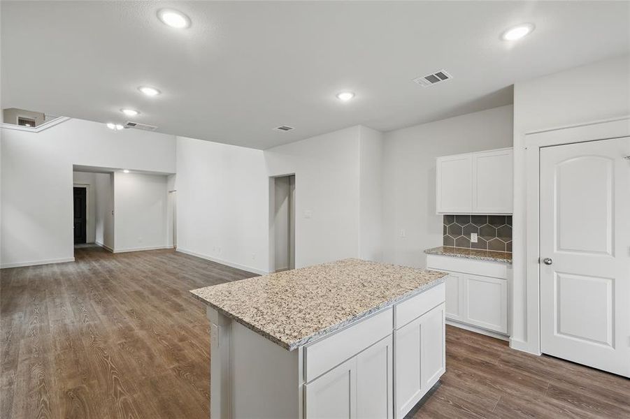 Kitchen featuring light stone counters, a center island, visible vents, decorative backsplash, and dark wood-type flooring Kitchen featuring light stone counters, a center island, visible vents, decorative backsplash, and dark wood-type flooring