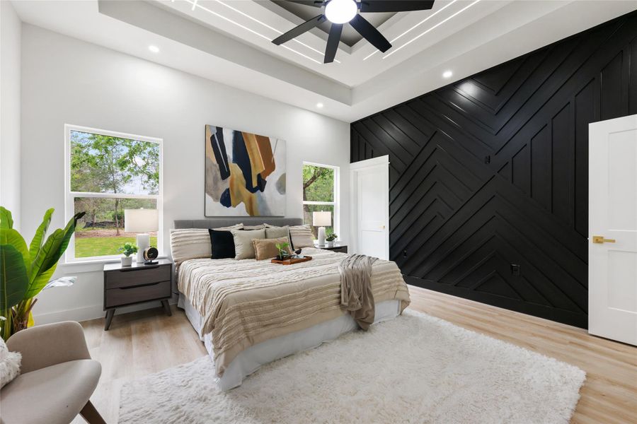 Accent wall with geometric paneling, tray ceiling with recessed lighting, wood-finish flooring, and multiple windows