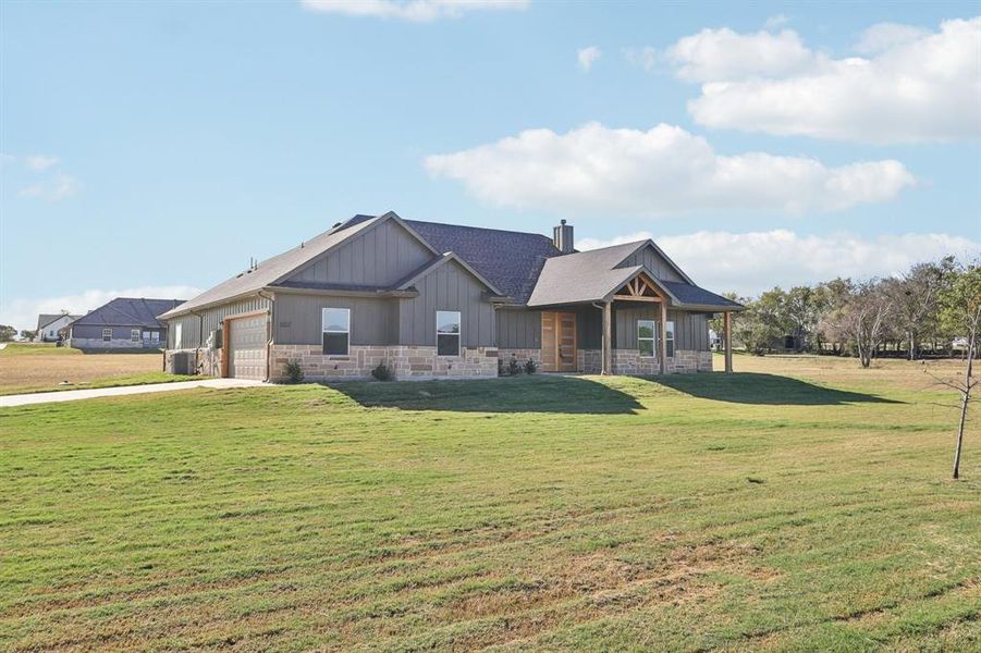 Craftsman inspired home featuring stone siding, board and batten siding, a front yard, a chimney, and an attached garage Craftsman inspired home featuring stone siding, board and batten siding, a front yard, a chimney, and an attached garage