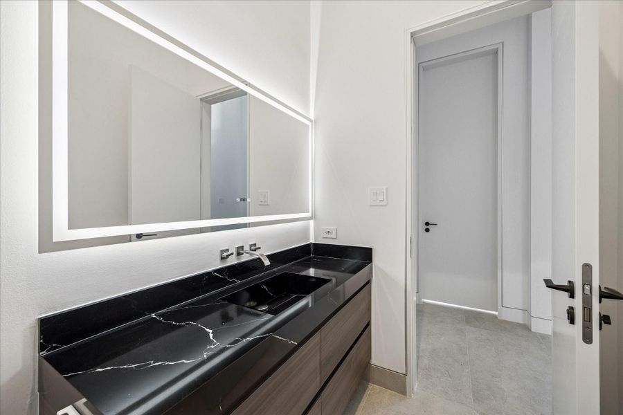 The downstairs powder room is complete with black marble counter tops and a light-up mirror.