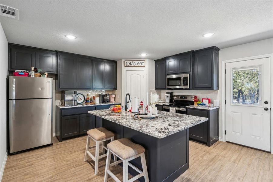 Kitchen with light stone counters, a kitchen island with sink, a breakfast bar, appliances with stainless steel finishes, and light wood-type flooring