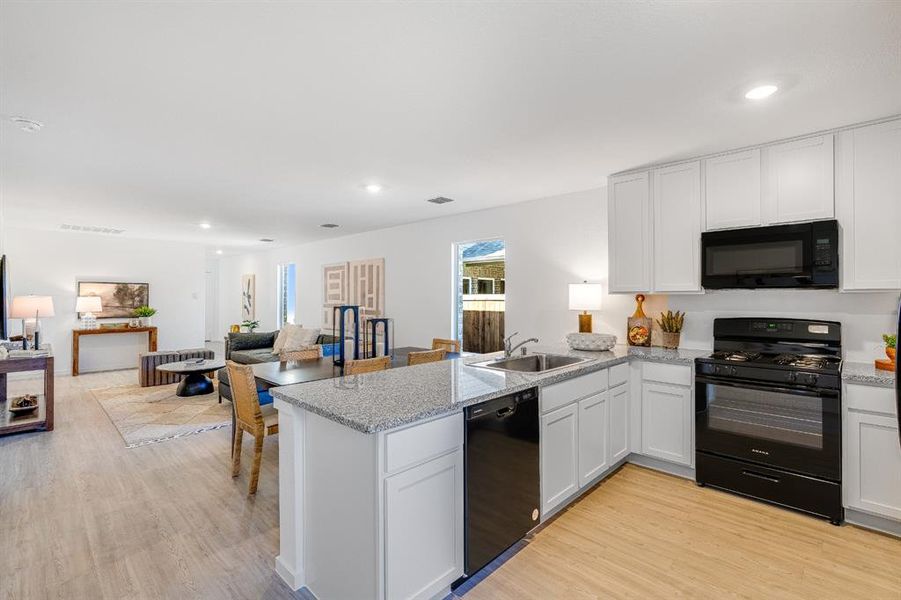 Kitchen featuring open floor plan, black appliances, white cabinets, light wood-style flooring, and recessed lighting