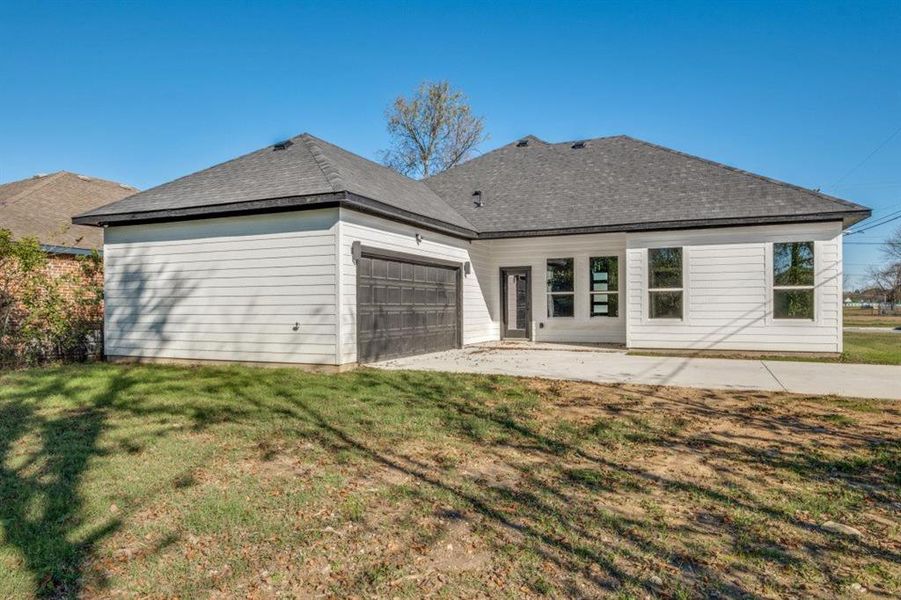 Rear view of property with a patio area, a lawn, roof with shingles, and an attached garage
