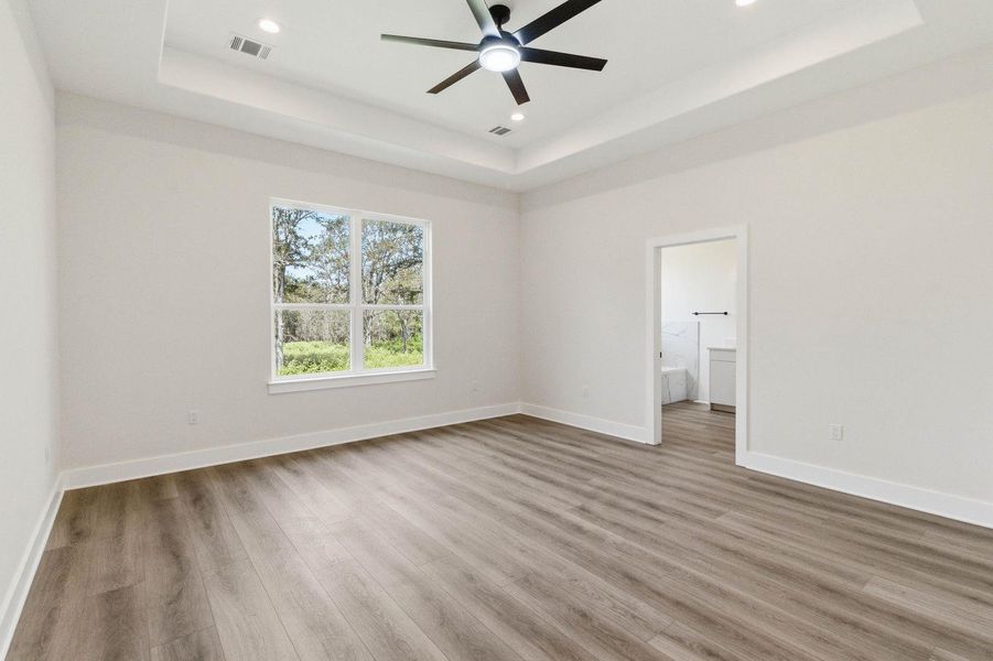 Elegant tray ceilings and resilient vinyl plank flooring define this expansive primary bedroom. Elegant tray ceilings and resilient vinyl plank flooring define this expansive primary bedroom.