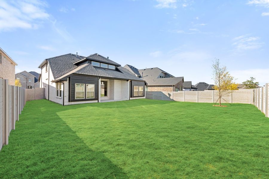 Backyard of a new home with large green lawn, wood privacy fence, and brick and dark siding exterior.