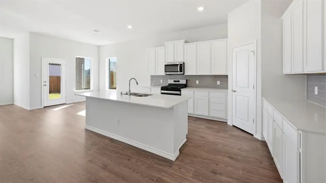 Contemporary kitchen featuring an island with an undermount sink, white cabinetry, integrated stainless steel appliances, a tiled backsplash, and wood-finish flooring