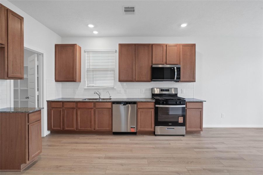 A true chef’s dream, this expansive kitchen boasts high ceilings, rich stained Woodmont Cody cabinets in Toffee stain, Granite countertops in Azul Plantino, gorgeous Daltile backsplash, stainless steel appliances, recessed lighting, extended counter space, and a pantry—all with a clear view of the spacious family room.