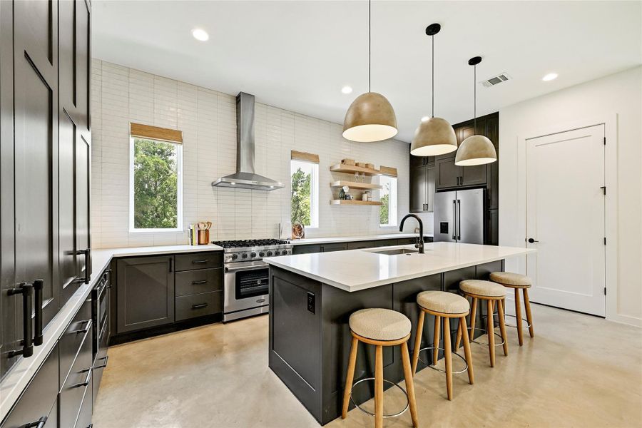 Chef's kitchen with oversized dark island, pendant lights, and open shelving. Chef's kitchen with oversized dark island, pendant lights, and open shelving.