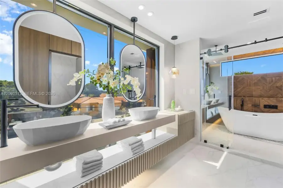 Floating dual-vanity featuring rectangular vessel sinks and pendant-style mirrors, paired with a glass-enclosed soaking tub and stone-tile flooring Floating dual-vanity featuring rectangular vessel sinks and pendant-style mirrors, paired with a glass-enclosed soaking tub and stone-tile flooring