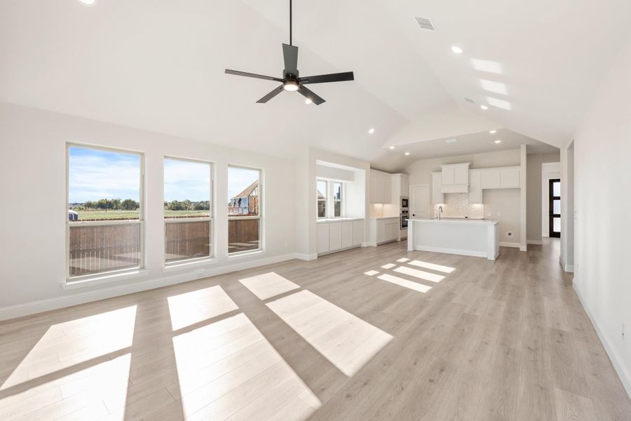Open-concept living area with vaulted ceiling, ceiling fan, light wood floors, and white kitchen with island.