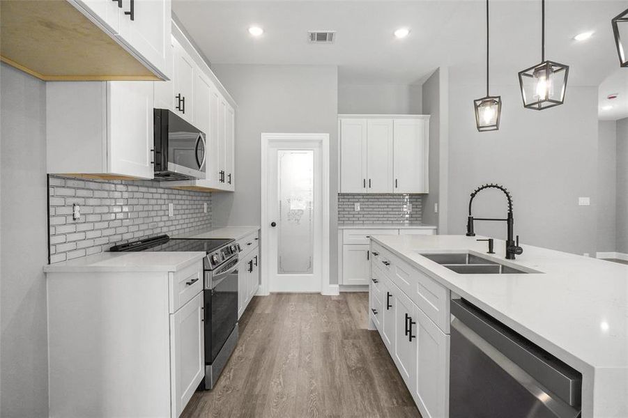 Kitchen featuring stainless steel appliances, wood finished floors, decorative backsplash, light countertops, and a kitchen island with sink Kitchen featuring stainless steel appliances, wood finished floors, decorative backsplash, light countertops, and a kitchen island with sink