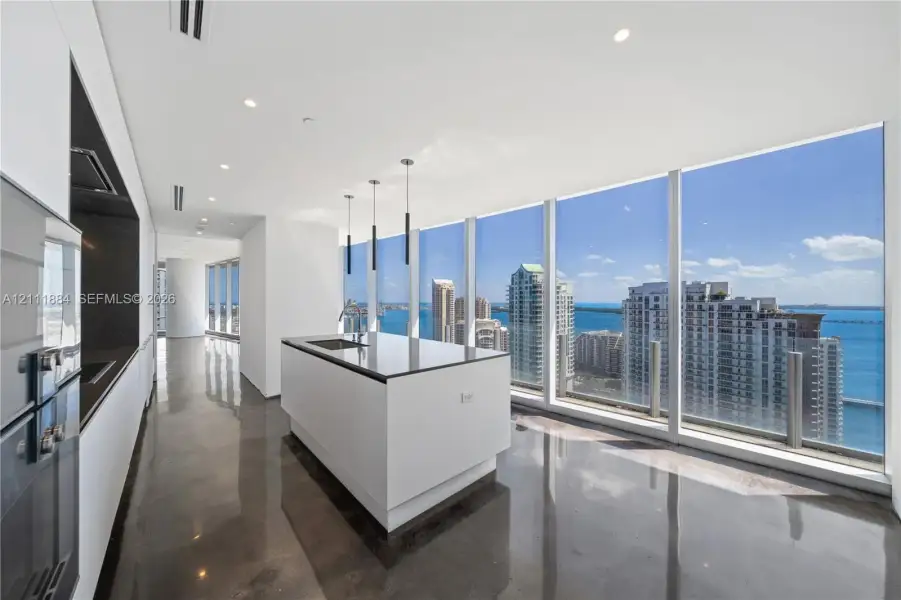 Modern kitchen featuring floor-to-ceiling windows, polished concrete flooring, a central island with a stone-surfaced countertop, integrated cabinetry, and recessed lighting Modern kitchen featuring floor-to-ceiling windows, polished concrete flooring, a central island with a stone-surfaced countertop, integrated cabinetry, and recessed lighting