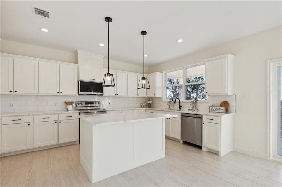 Kitchen with white cabinets, appliances with stainless steel finishes, sink, a kitchen island, and tasteful backsplash