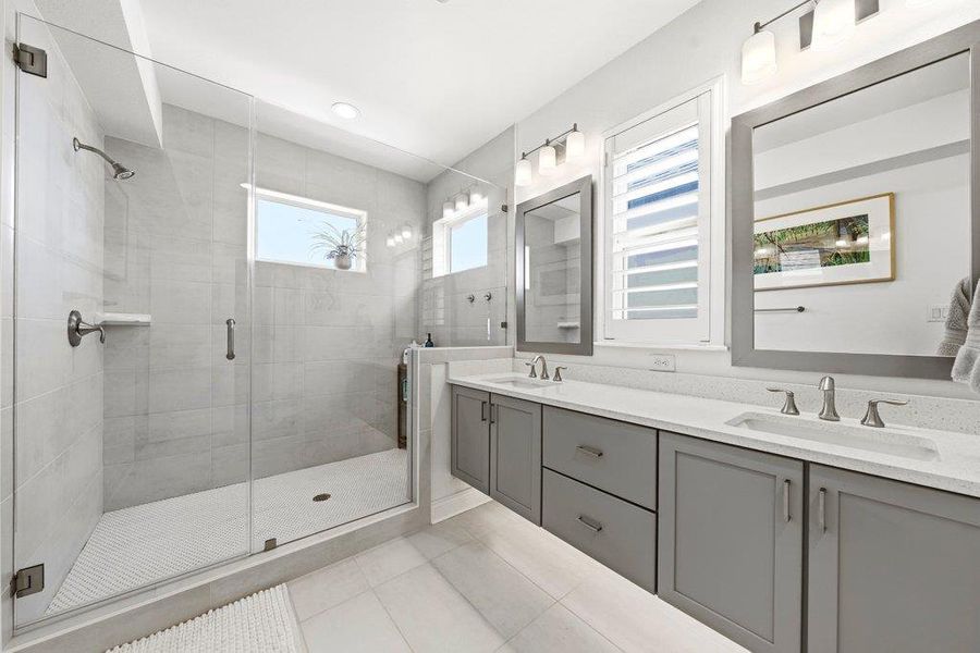 A modern double vanity stands opposite a glass-enclosed shower with pristine tile finishes. A modern double vanity stands opposite a glass-enclosed shower with pristine tile finishes.