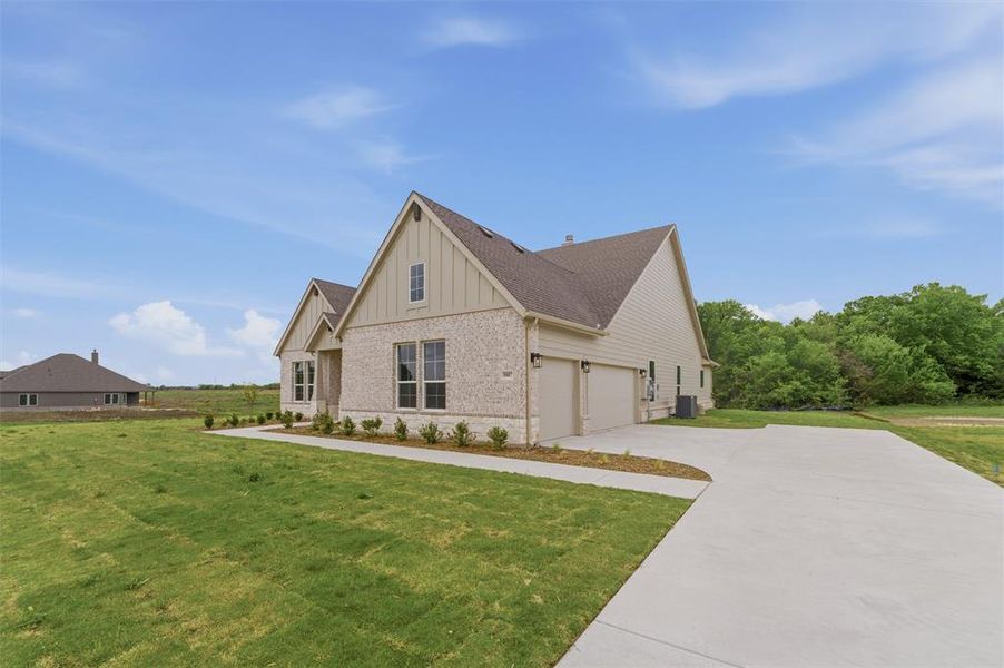 View of property exterior with board and batten siding, brick siding, a lawn, and concrete driveway