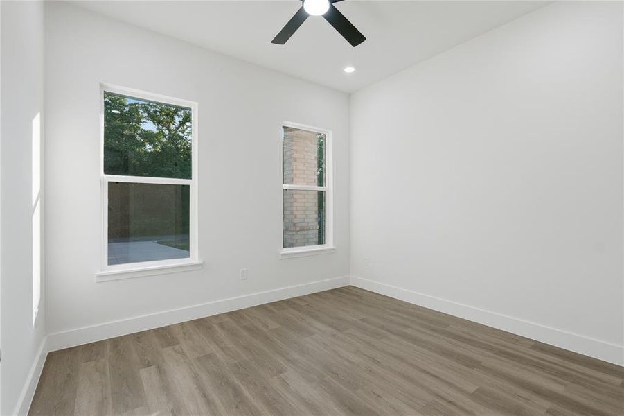 Neutral-toned room featuring two windows, wood-finish flooring, recessed lighting, and a ceiling fan