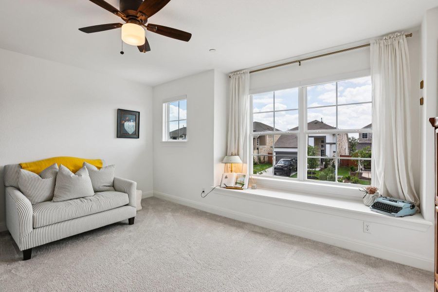 Well-lit room featuring a large window with a built-in window seat, a smaller window, and a ceiling fan