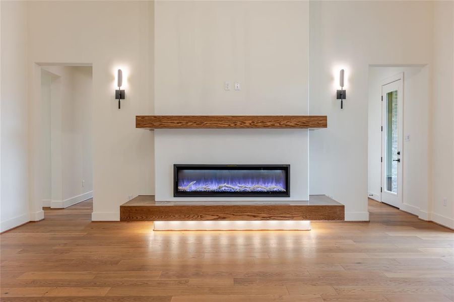 Living room with a glass covered fireplace, light wood finished floors, and a towering ceiling