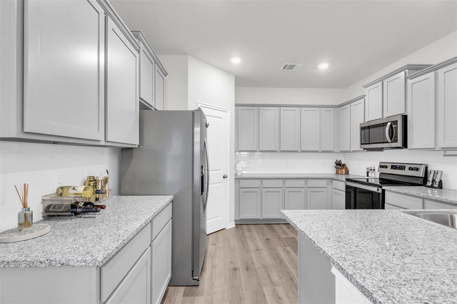 Kitchen with appliances with stainless steel finishes, light wood finished floors, decorative backsplash, recessed lighting, and gray cabinetry Kitchen with appliances with stainless steel finishes, light wood finished floors, decorative backsplash, recessed lighting, and gray cabinetry
