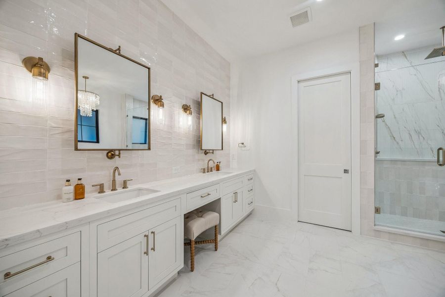Primary Bath with 12 x 24 Marble Dolomite White Tile Floor.  Inset Shaker Style Cabinetry with Soft Close Drawers and Doors. Long Double Vanity with Slab Quartz Counter and a 3 x 9 Glazed Tile Backsplash/Wall. Dual Rectangle Sinks, Dual Widespread Faucets in a Champagne Bronze Finish, Dual Pivot Mirrors with Champagne Gold Finish, Four 1 Light Clear Fluted Glass Sconces in a Heritage Brass Finish.  There is also a knee space and Separate Commode Area.