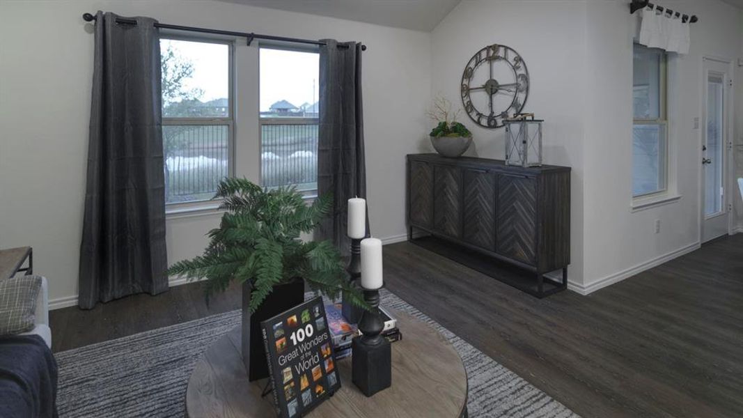 Spacious living area featuring wood-finish flooring, light neutral wall tones, and a pair of large windows with dark drapery panels Spacious living area featuring wood-finish flooring, light neutral wall tones, and a pair of large windows with dark drapery panels