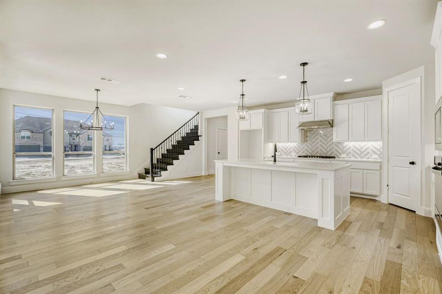 Kitchen featuring a kitchen island with sink, light wood-style flooring, hanging lights, open floor plan, and white cabinets