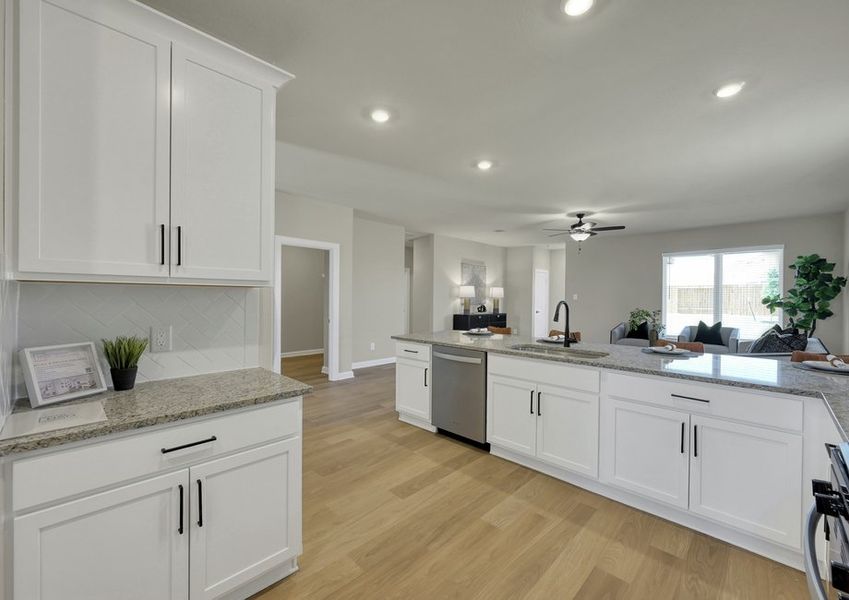 Wide kitchen view showing white cabinetry, granite countertops, stainless appliances, and an open sightline to the living area.