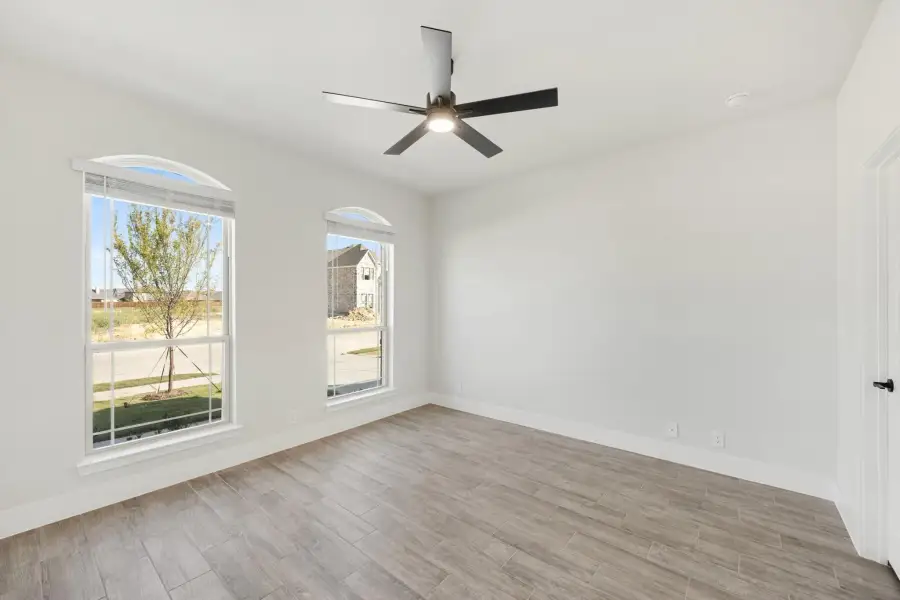 Empty room with wood-look tile floors, black ceiling fan, and two arched windows with natural light