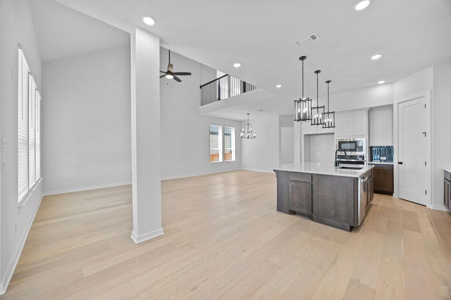 Kitchen with built in microwave, ceiling fan, light countertops, open floor plan, and a chandelier