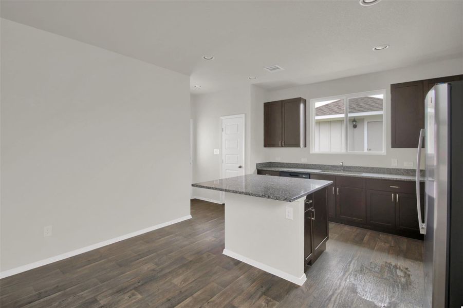 Kitchen featuring freestanding refrigerator, dark wood finish cabinetry, dark wood-style flooring, a kitchen island, and recessed lighting