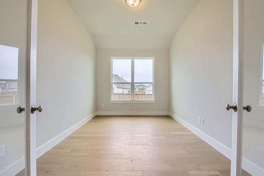 Empty room with light wood-type flooring, french doors, and vaulted ceiling
