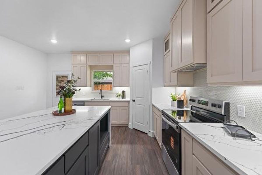 Kitchen featuring a large central island with a stone countertop, wood-finish flooring, recessed lighting, stainless steel appliances, and light-toned cabinetry with under-cabinet lighting Kitchen featuring a large central island with a stone countertop, wood-finish flooring, recessed lighting, stainless steel appliances, and light-toned cabinetry with under-cabinet lighting