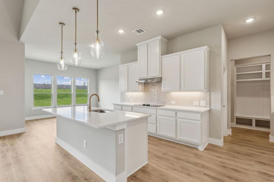 Kitchen with hanging light fixtures, a kitchen island with sink, sink, and white cabinetry