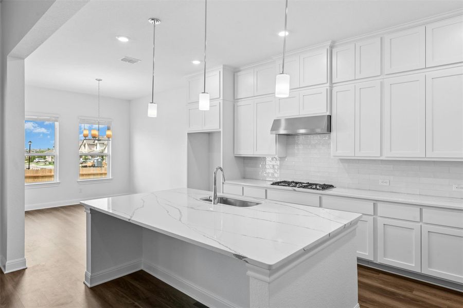 A well-lit kitchen boasts pristine white cabinetry, quartz countertops, and sleek pendant lighting.