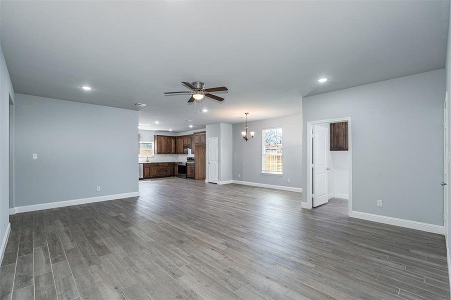 Unfurnished living room featuring recessed lighting, dark wood finished floors, baseboards, and ceiling fan with notable chandelier