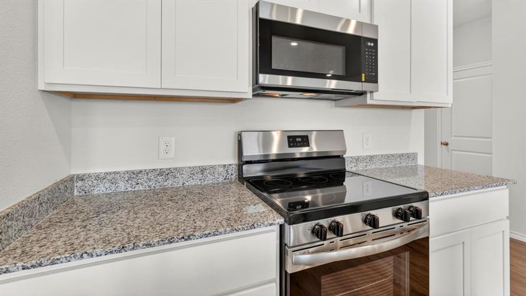 Modern kitchen featuring a stainless steel electric range, an over-the-range microwave, white shaker-style cabinetry, and speckled countertops
