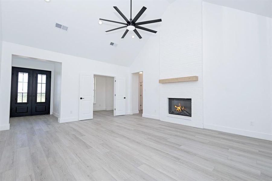 Unfurnished living room featuring high vaulted ceiling, a ceiling fan, french doors, a large fireplace, and light wood finished floors