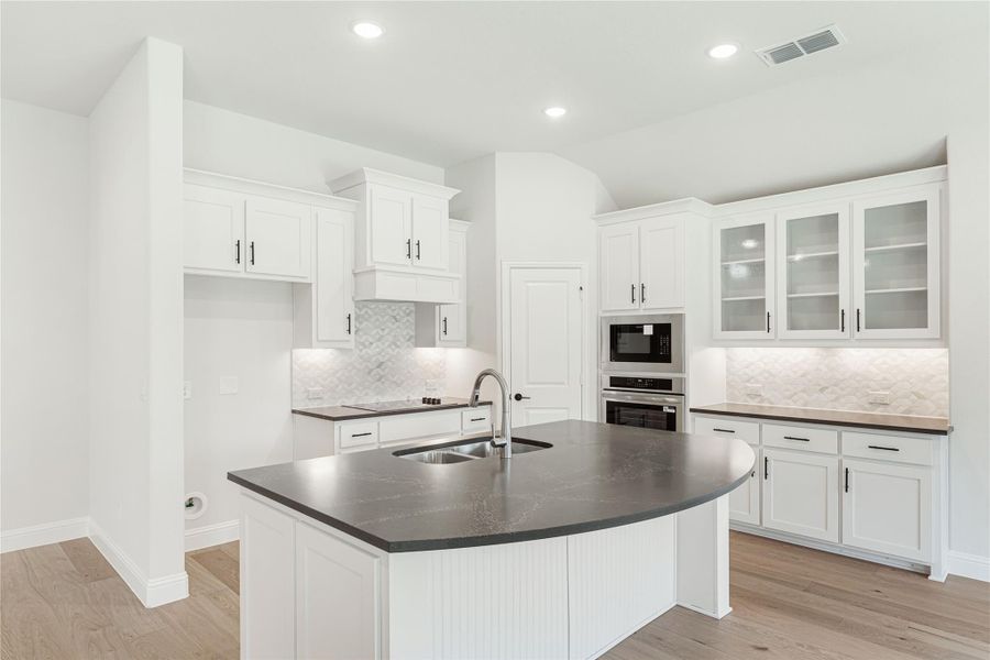Kitchen with white cabinets, curved island with dark countertop, stainless steel appliances, and light wood floors